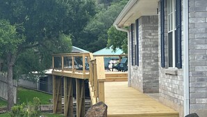 A wooden deck leading to a house with a stone facade and blue shutters. - Scenic views on a quiet fishing cove. Boat Slip, Kayaks, Peddle Boat, SUPs. (Sunrise Beach Village)