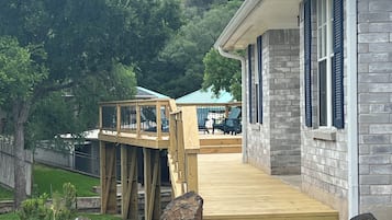 A wooden deck leading to a house with a stone facade and blue shutters.