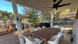 A covered outdoor patio with a wooden table and white chairs, a ceiling fan, and a view of a backyard with a barbecue grill. - Scenic views on a quiet fishing cove. Boat Slip, Kayaks, Peddle Boat, SUPs. (Sunrise Beach Village)