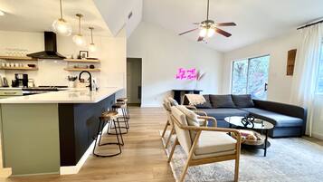 A modern kitchen with a central island, bar stools, pendant lighting, and a ceiling fan.
