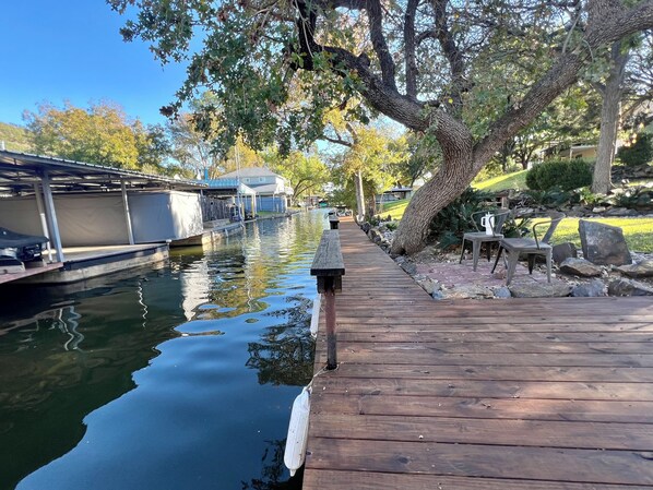 A wooden dock extending into a calm body of water, with boats docked on the left and a picnic table with chairs on the right.
