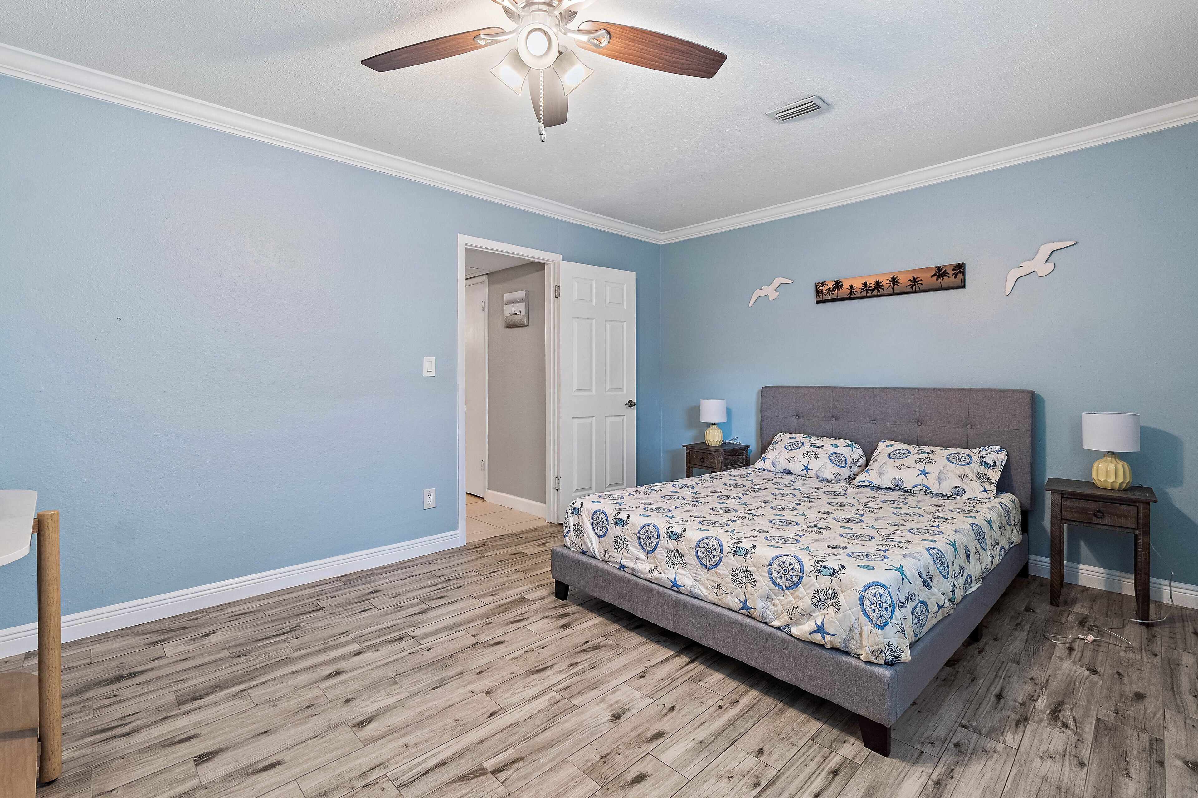 A bedroom with a bed, a ceiling fan, a nightstand, and a door leading to another room.