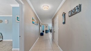 A hallway with beige walls, a light blue accent wall, and a wooden floor. There are framed pictures on the walls, a ceiling light, and a door on the right. - Near Tesla's Building - Centralized location (St. Petersburg)