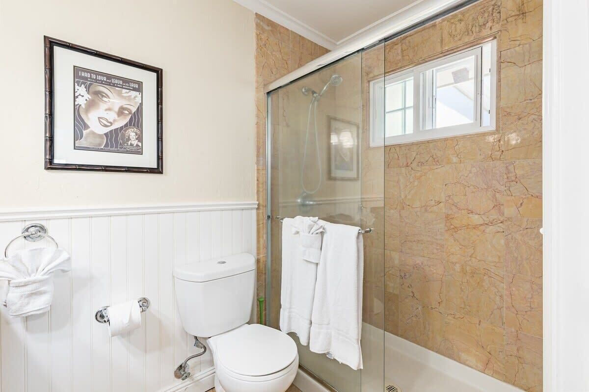 A bathroom with a toilet, a glass-enclosed shower, a framed picture on the wall, and a towel rack.