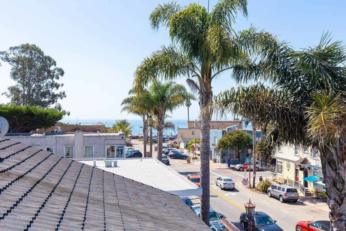 A street view with palm trees, parked cars, and buildings.