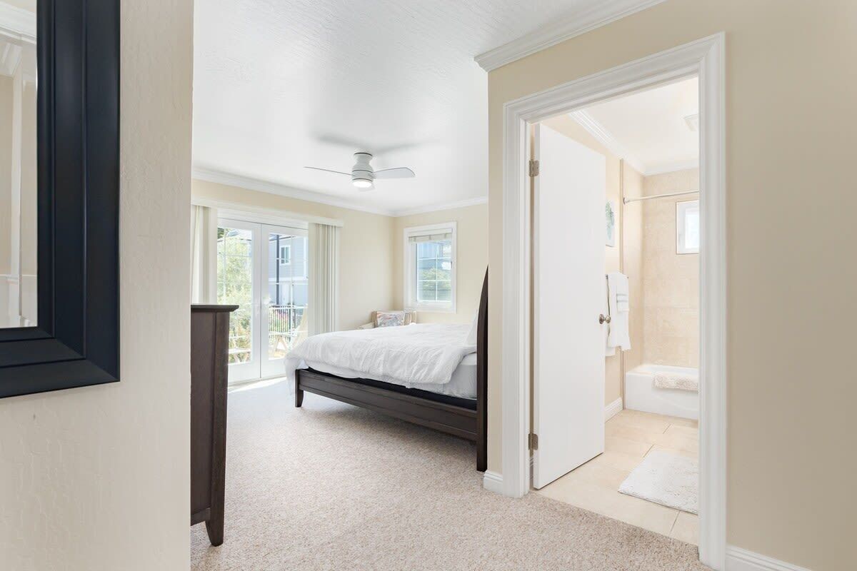 A bedroom with a bed, a ceiling fan, and a bathroom visible through an open door.