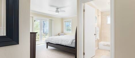 A bedroom with a bed, a ceiling fan, and a bathroom visible through an open door.