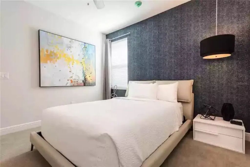 Ein modernes Schlafzimmer mit einem großen Bett, einem Nachttisch, einer Wandlampe und einem großen abstrakten Gemälde.