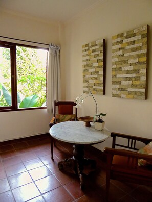 A room with a round table, chairs, a window with curtains, and a wall with a brick pattern.