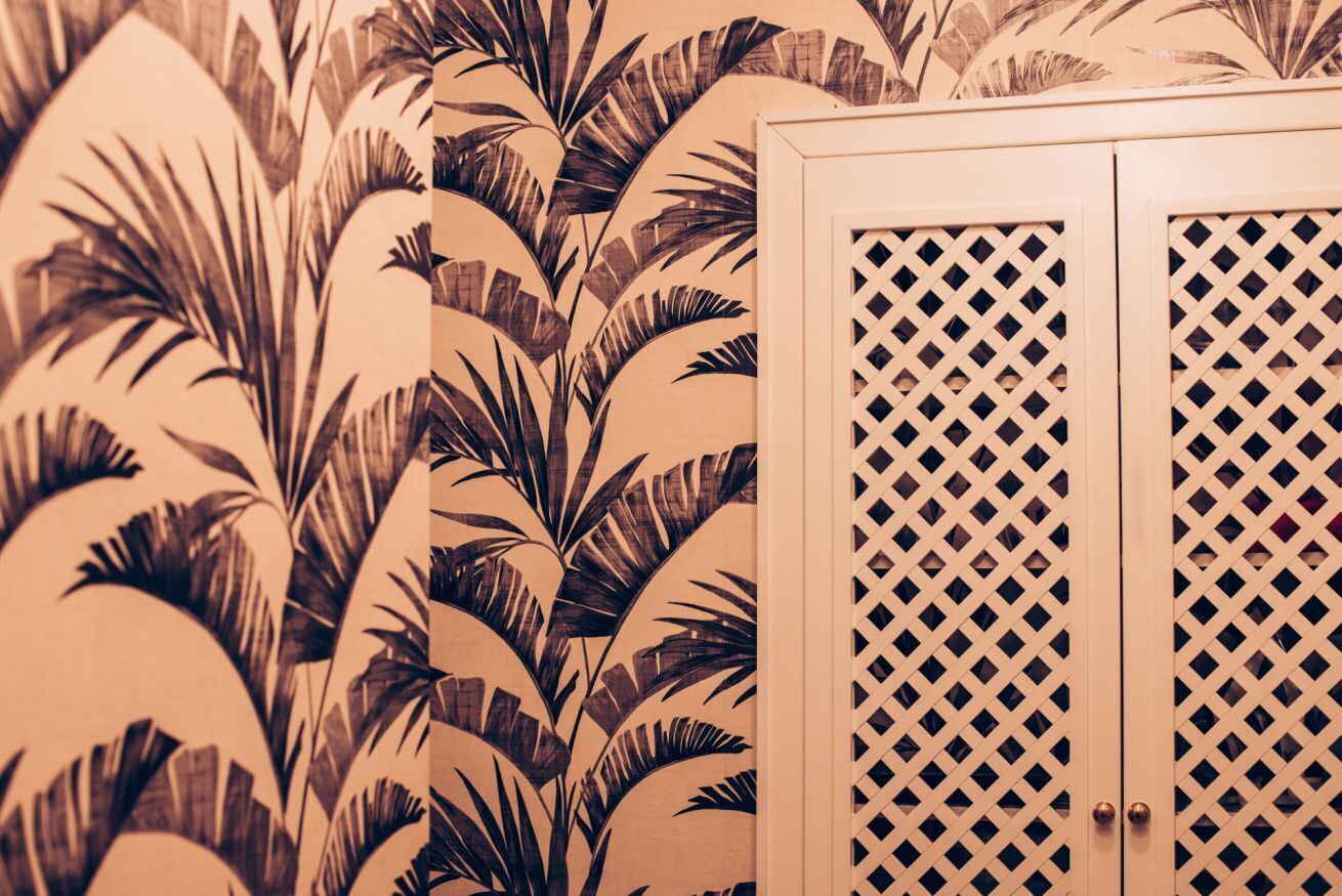 A room with a patterned wallpaper featuring palm leaves and a wooden cabinet with a lattice design.