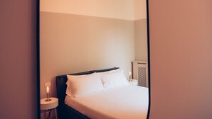 Ein ordentlich gemachtes Bett mit weißen Leinentüchern und einem dunklen Kopfteil in einem Hotelzimmer.