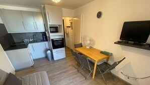 A compact living space with a kitchenette, a dining area with a table and chairs, a sofa, a TV mounted on the wall, and a trash bin. - 1 bedroom apartment close to the beach of Les Sablettes (LA SEYNE SUR MER)