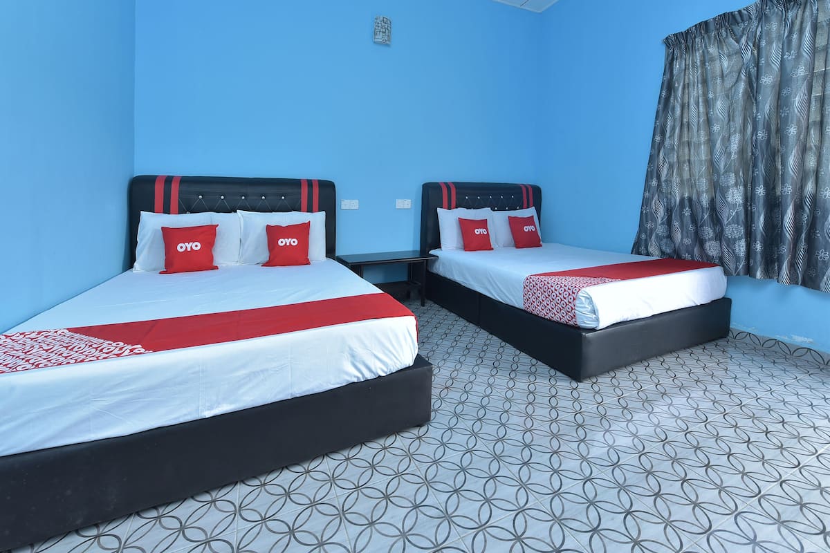 Ein Hotelzimmer mit zwei Betten, jeweils mit schwarzem Kopfteil und Bettwäsche in Rot und Weiß. Die Wände sind blau und der Boden ist gemustert.