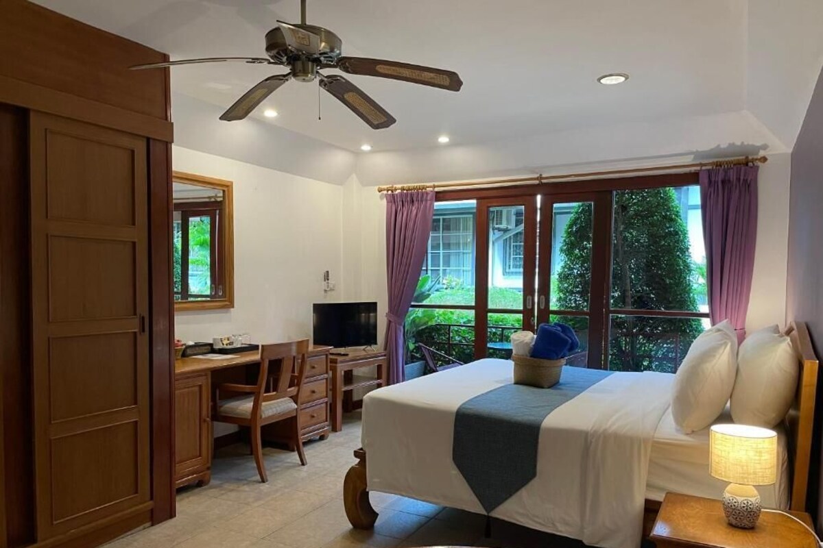 A hotel room with a bed, desk, chair, and a ceiling fan.
