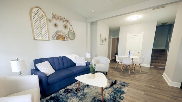 A modern living room with a blue sofa, white armchairs, a white coffee table, and a dining area with a white table and chairs.