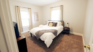 A bedroom with a bed, a bedside table, a lamp, and a window with curtains.