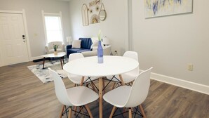 A modern living room with a round white table, white chairs, a blue sofa, and a decorative wall piece.