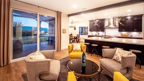 Un salon moderne avec une porte vitrée donnant sur un patio, une cuisine avec des meubles sombres et un coin bar, et un fauteuil jaune.