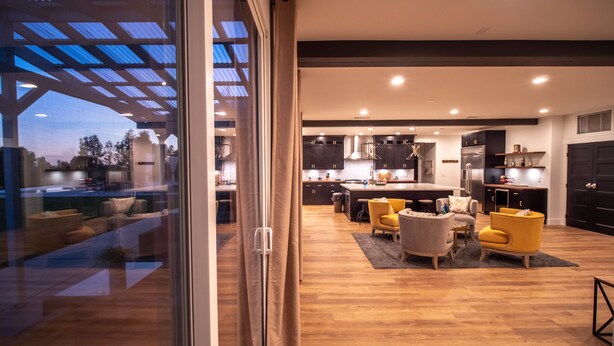 Une cuisine moderne avec des meubles de couleur sombre, un îlot central et un coin repas doté de chaises jaunes.