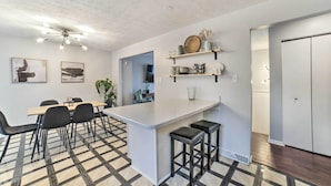 A modern kitchen with a central island, black bar stools, and a dining area with a checkered floor. - Pittsburgh Retreat w/ Deck ~ 4 Mi to Dtwn! (Pittsburgh)
