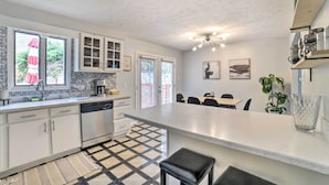 A modern kitchen with white cabinets, a large island, and a dining area with a table and chairs. - Pittsburgh Retreat w/ Deck ~ 4 Mi to Dtwn! (Pittsburgh)