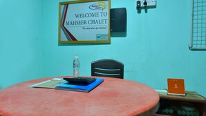 A room with a round table, a chair, a water bottle, a notebook, a pen, a signboard, and a power outlet.