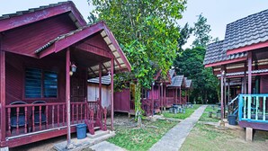 A row of wooden cabins with red exteriors and blue railings, each featuring a porch and a small front yard.