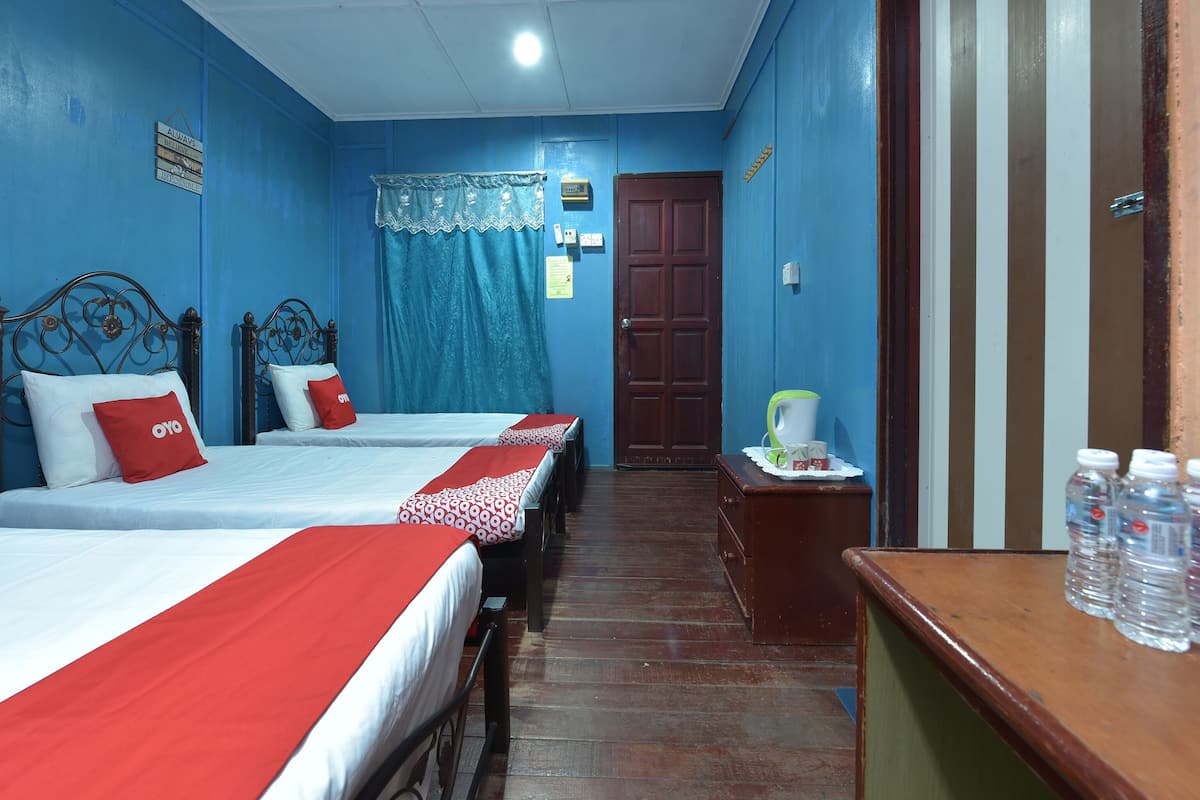 Une chambre d’hôtel avec deux lits, une commode en bois, une petite table avec une bouilloire et des tasses, et une porte à motifs rayés.