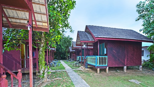 A row of traditional wooden houses with red exteriors and blue railings, connected by a narrow pathway.