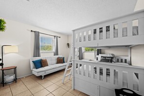 A room with a bunk bed, a sofa, a small table, and a window with curtains.