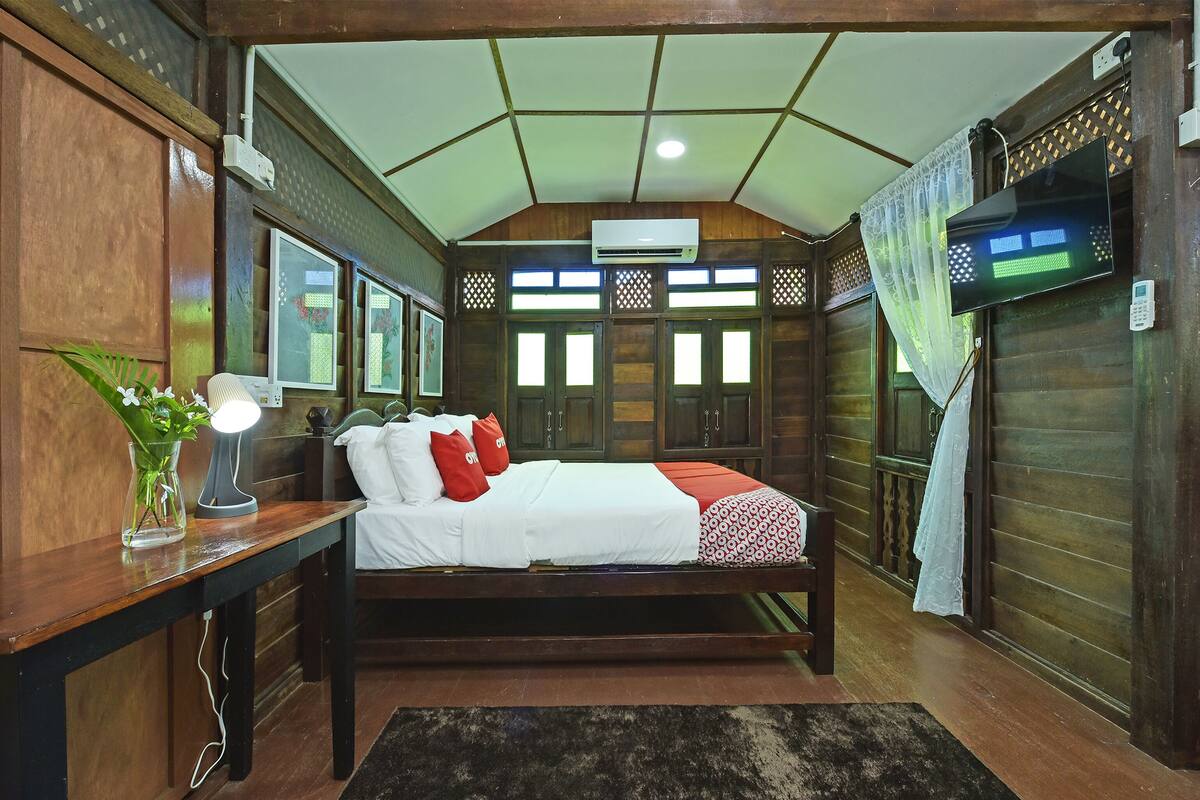 A bedroom with a wooden bed, a bedside table with a lamp, a small plant, and a window with a view of the outside.