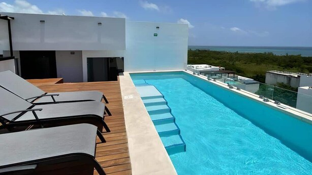 A rooftop pool with clear blue water, wooden deck, and lounge chairs.