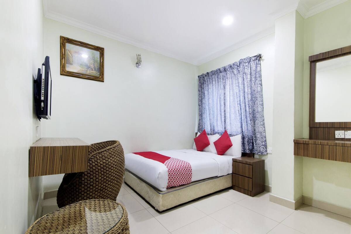 A bedroom with a bed, bedside table, chair, and a television mounted on the wall.