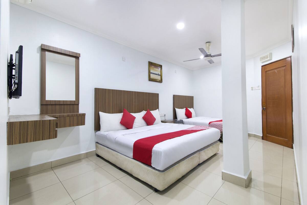 A hotel room with a large bed, a wooden headboard, a mirror, a ceiling fan, and a door.
