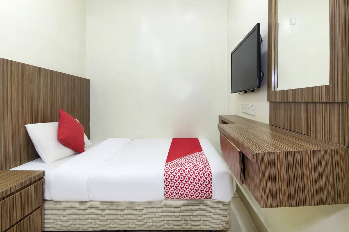 A hotel room with a bed, a TV mounted on the wall, and a wooden headboard.