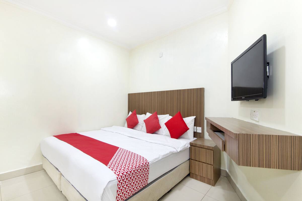 A hotel room with a bed, a TV mounted on the wall, and a wooden bedside table.