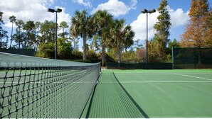 Un court de tennis avec un filet, entouré d’arbres et sous un ciel dégagé.