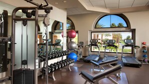Une salle de sport équipée de tapis de course, de vélos elliptiques, de poids libres et de ballons d’exercice.