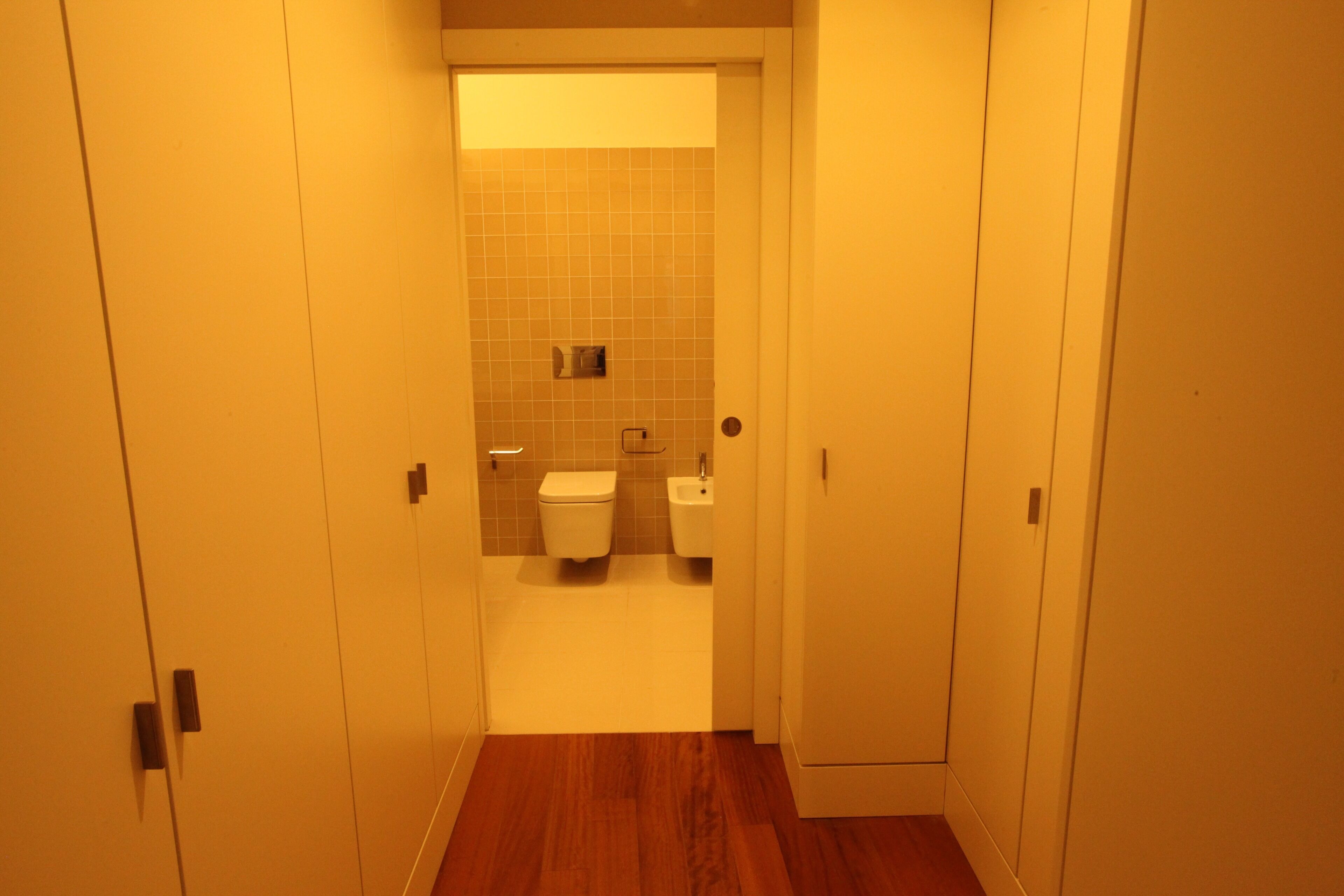 A narrow hallway leading to a bathroom with a toilet and bidet.