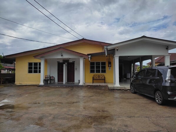 A two-story building with a yellow facade, a covered porch, and a car parked in the driveway. - OYO Homes 90600 Ummi Chalet Dungun (Dungun)