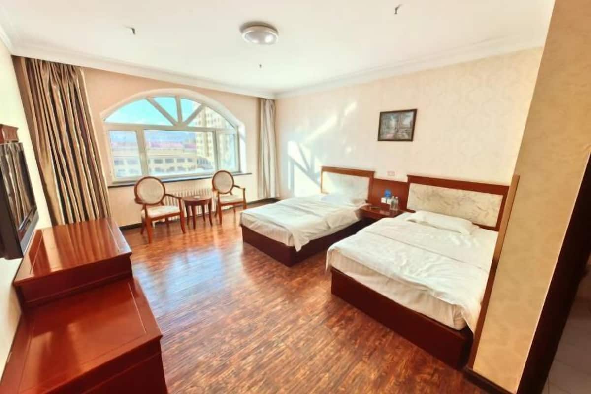 A hotel room with two beds, a desk, a chair, a window with a view, and a ceiling light.