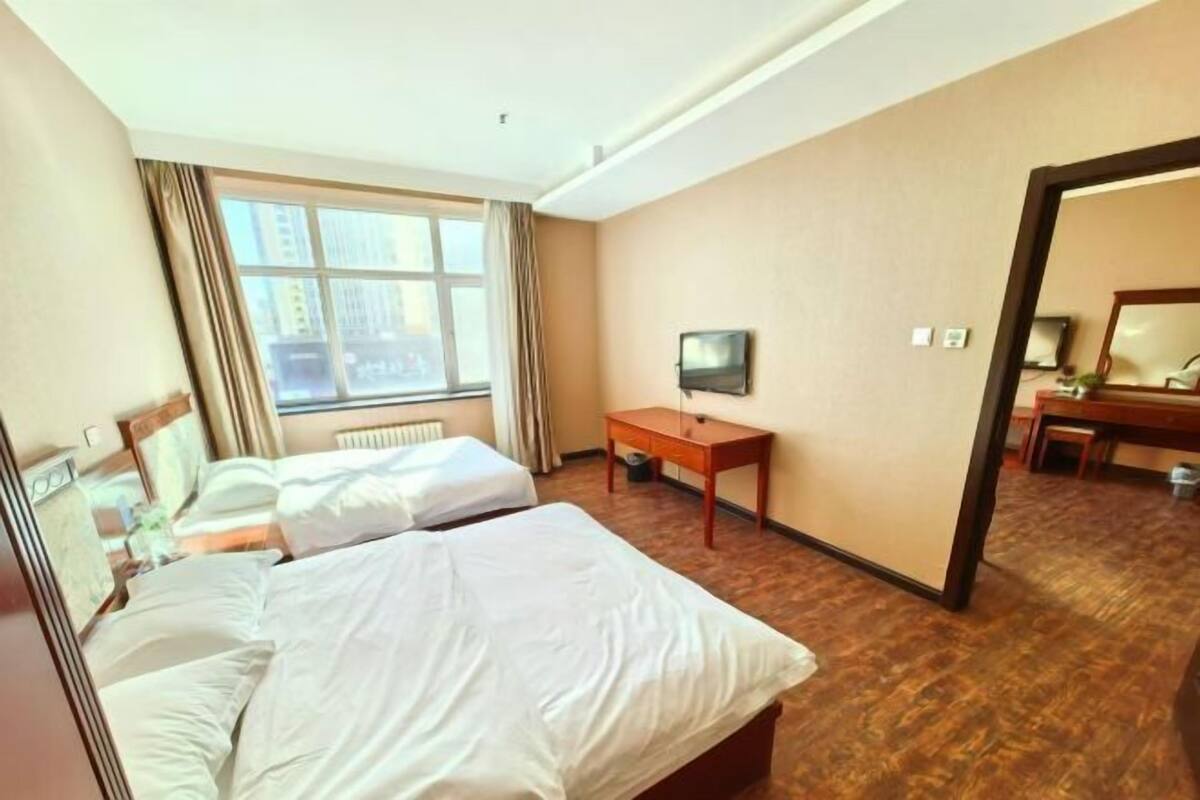 A hotel room with two beds, a television, a wooden desk, and a large mirror.