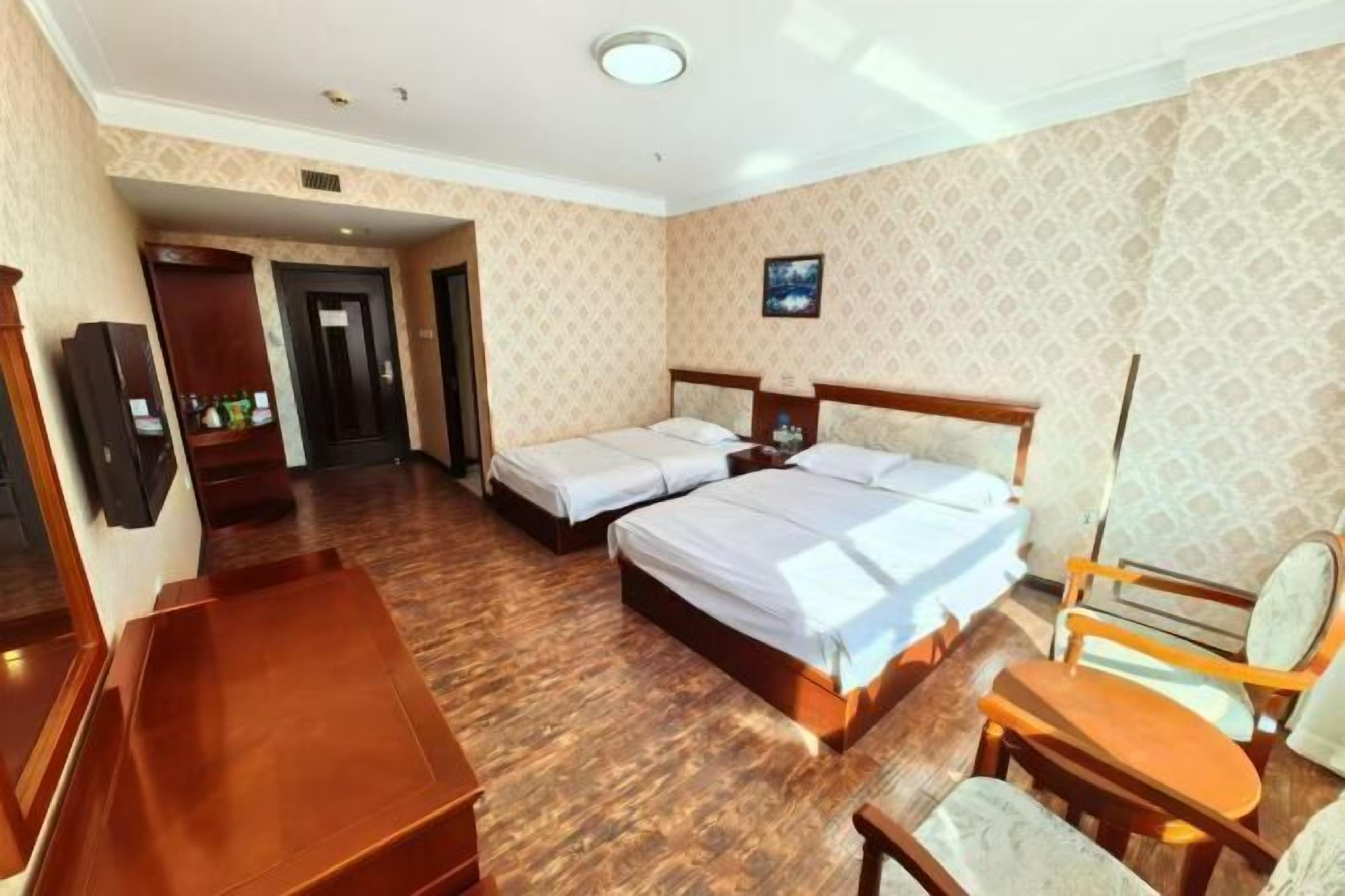 A hotel room with two beds, a desk, a chair, and a small table.