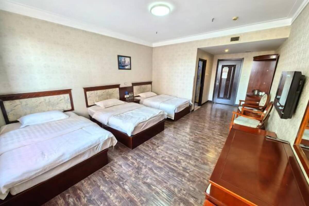 A hotel room with three beds, a wooden desk, and a television.