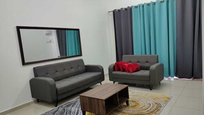 A living room with a grey sofa, a smaller grey armchair with a red pillow, a wooden coffee table, and a large mirror on the wall. - OYO Homes 90611 Homestay D'emas (Kuala Lipis)