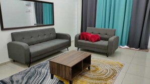 A living room with two grey sofas, a wooden coffee table, and a patterned rug. - OYO Homes 90611 Homestay D'emas (Kuala Lipis)