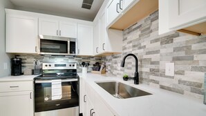 A modern kitchen with white cabinets, a stainless steel sink, a microwave, and a double oven. - Cheerful Townhouse - Walk to Table Rock Lake! (Kimberling City)