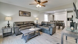A living room with a sectional sofa, a coffee table, and a ceiling fan. There is a dining area with a table and chairs. - Cheerful Townhouse - Walk to Table Rock Lake! (Kimberling City)