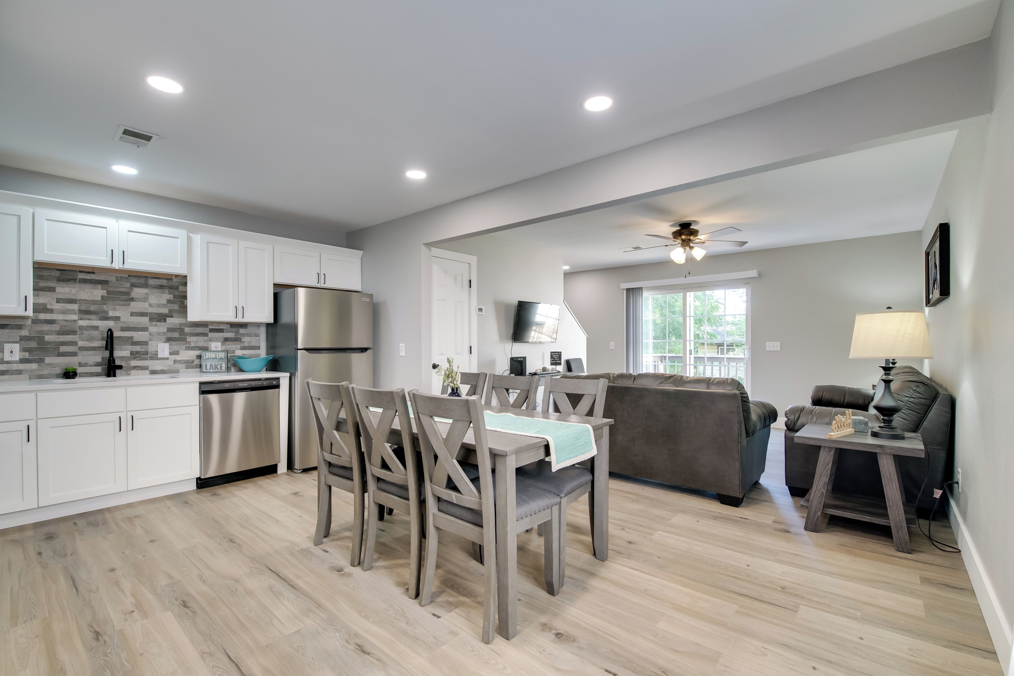 A modern kitchen with white cabinets, a stainless steel refrigerator, and a dining area with wooden chairs.