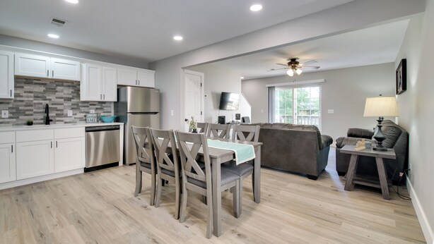 A modern kitchen with white cabinets, a stainless steel refrigerator, and a dining area with wooden chairs. - Cheerful Townhouse - Walk to Table Rock Lake! (Kimberling City)